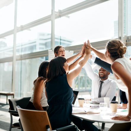 Shot of a group of businesspeople high fiving while sitting in a meeting