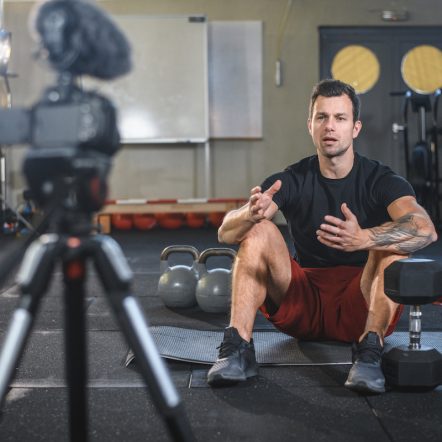 Male Athlete Sitting on Exercise Mat and Making Vlog at Gym